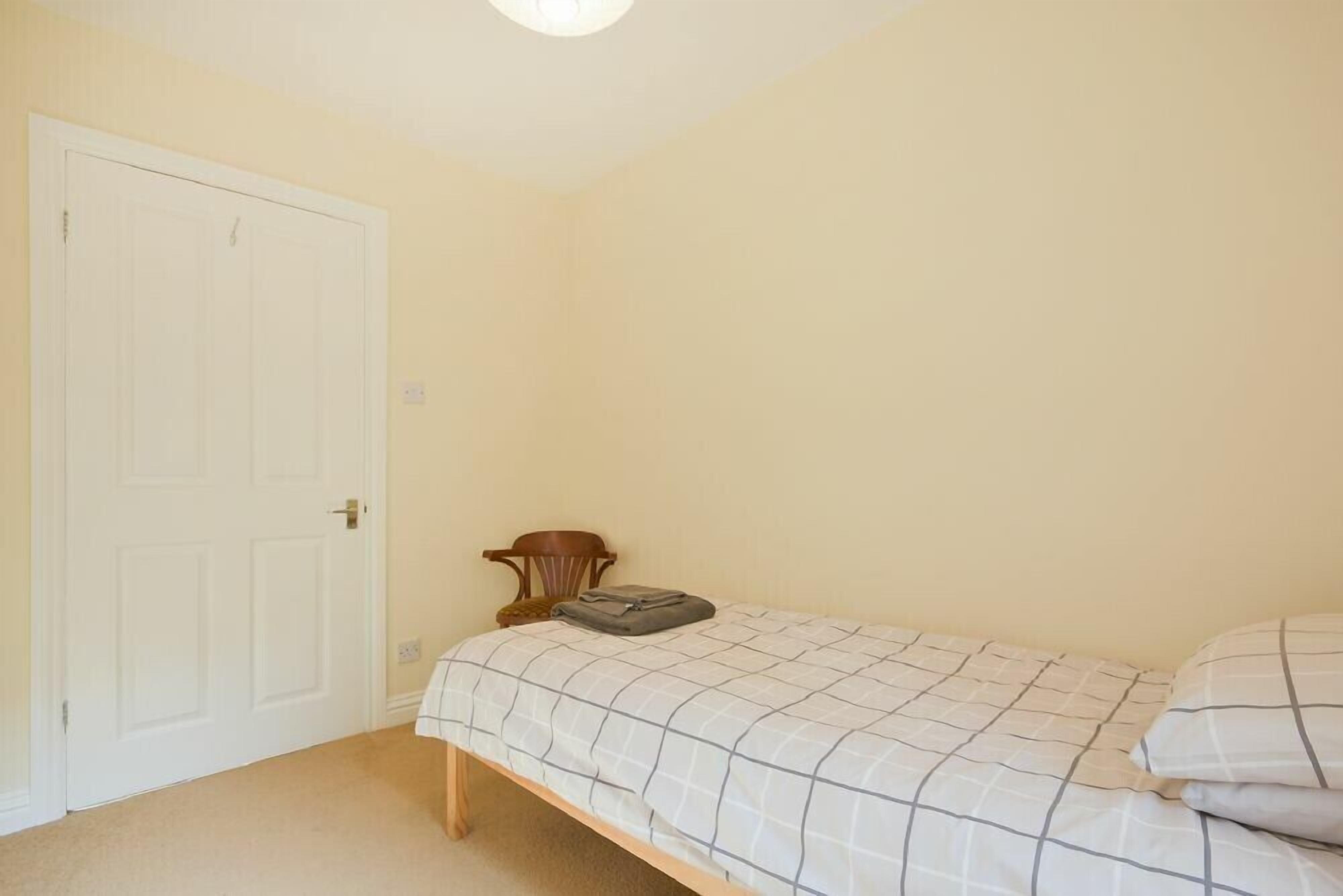 A bedroom with a single bed, a wooden chair, and a white door.