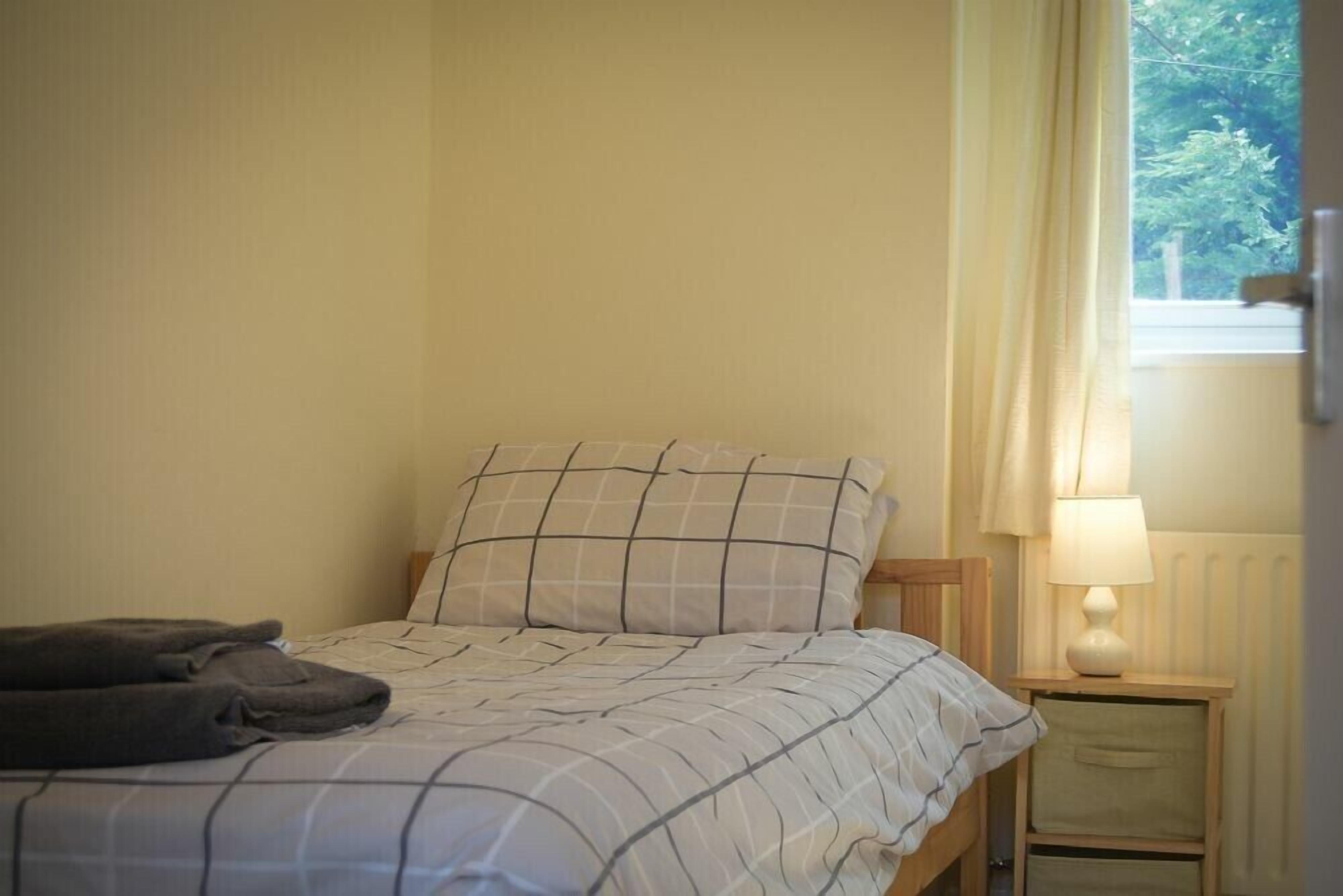 A single bed with a checkered bedspread, a bedside lamp, and a window with curtains.