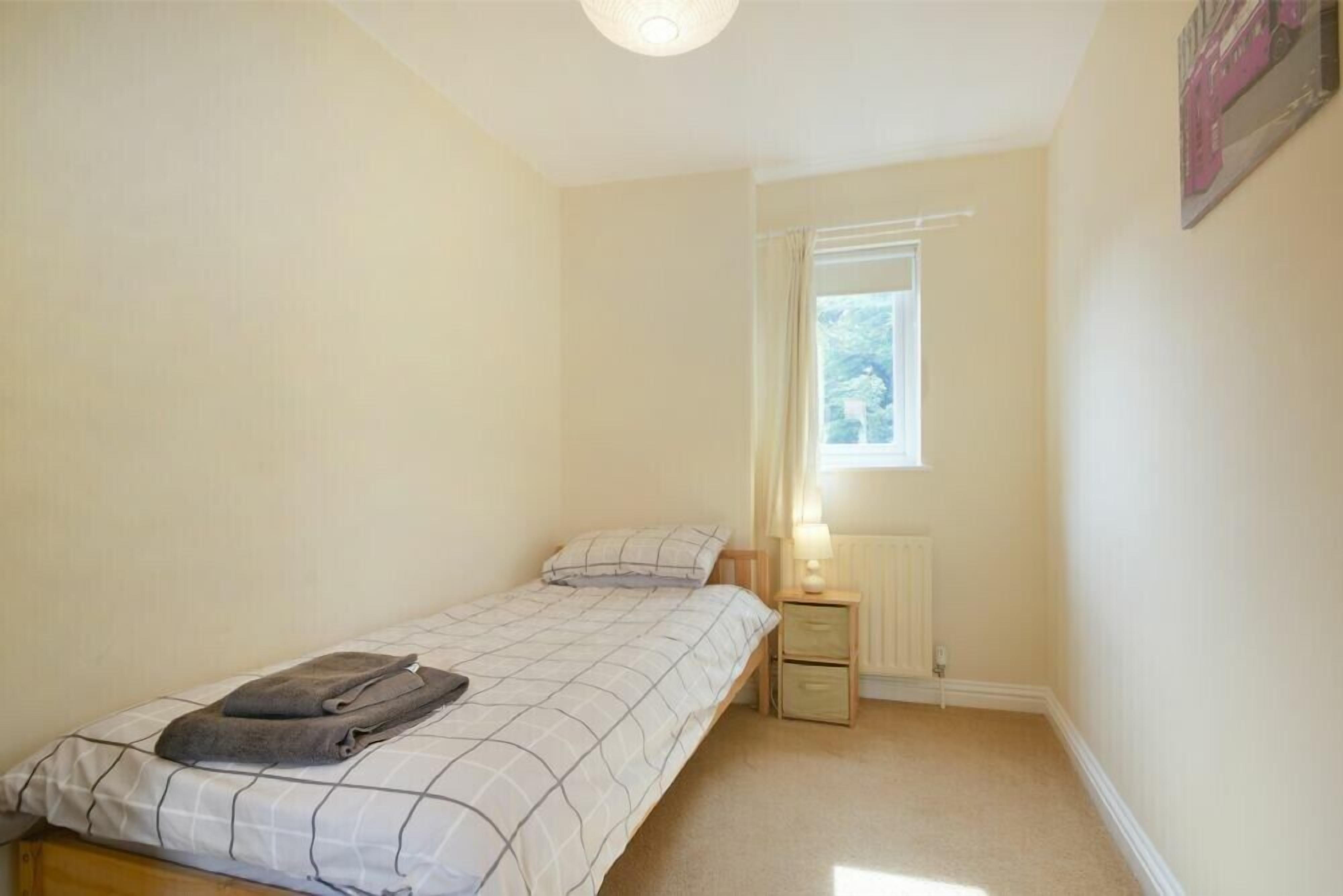 Een compacte, verzorgde slaapkamer met een eenpersoonsbed, nachtkastje, raam en radiator.