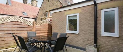 Une terrasse extérieure avec une table et des chaises, une clôture en bois et un bâtiment en briques doté de fenêtres.