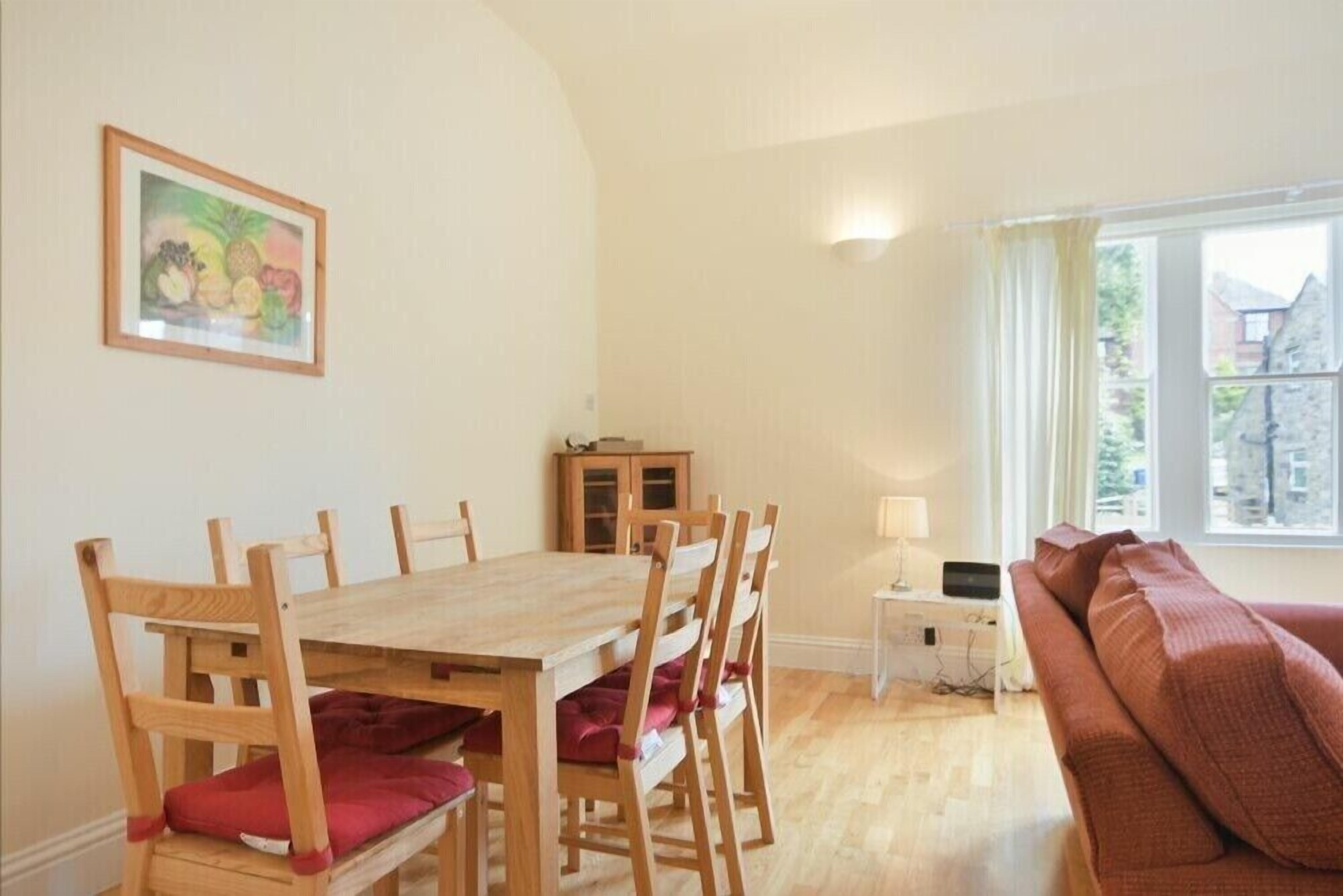 Un comedor con una mesa y sillas de madera, un armario, una lámpara y un sofá junto a una ventana.