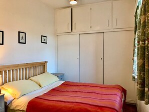 Quarto com cama, mesa de cabeceira, guarda-roupa e parede com quadros.