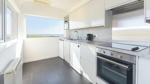 Eine moderne Küche mit weißen Schränken, einem eingebauten Ofen und Meerblick.