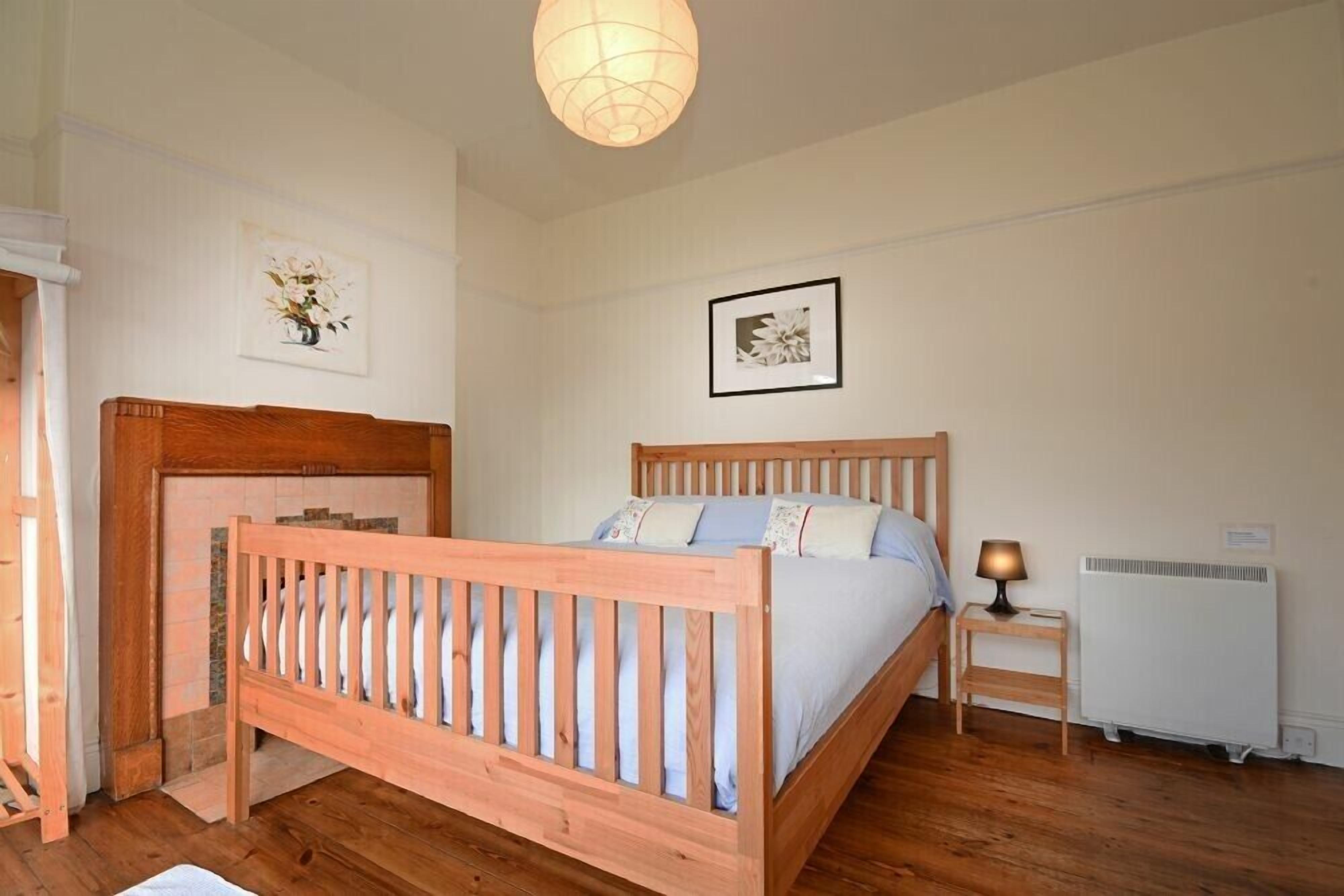 A bedroom with a wooden bed, a nightstand with a lamp, a radiator, and two framed pictures on the wall.