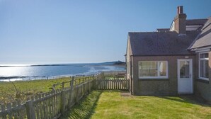 Ein Küstenhaus mit Holzzaun, Rasen und Meerblick.