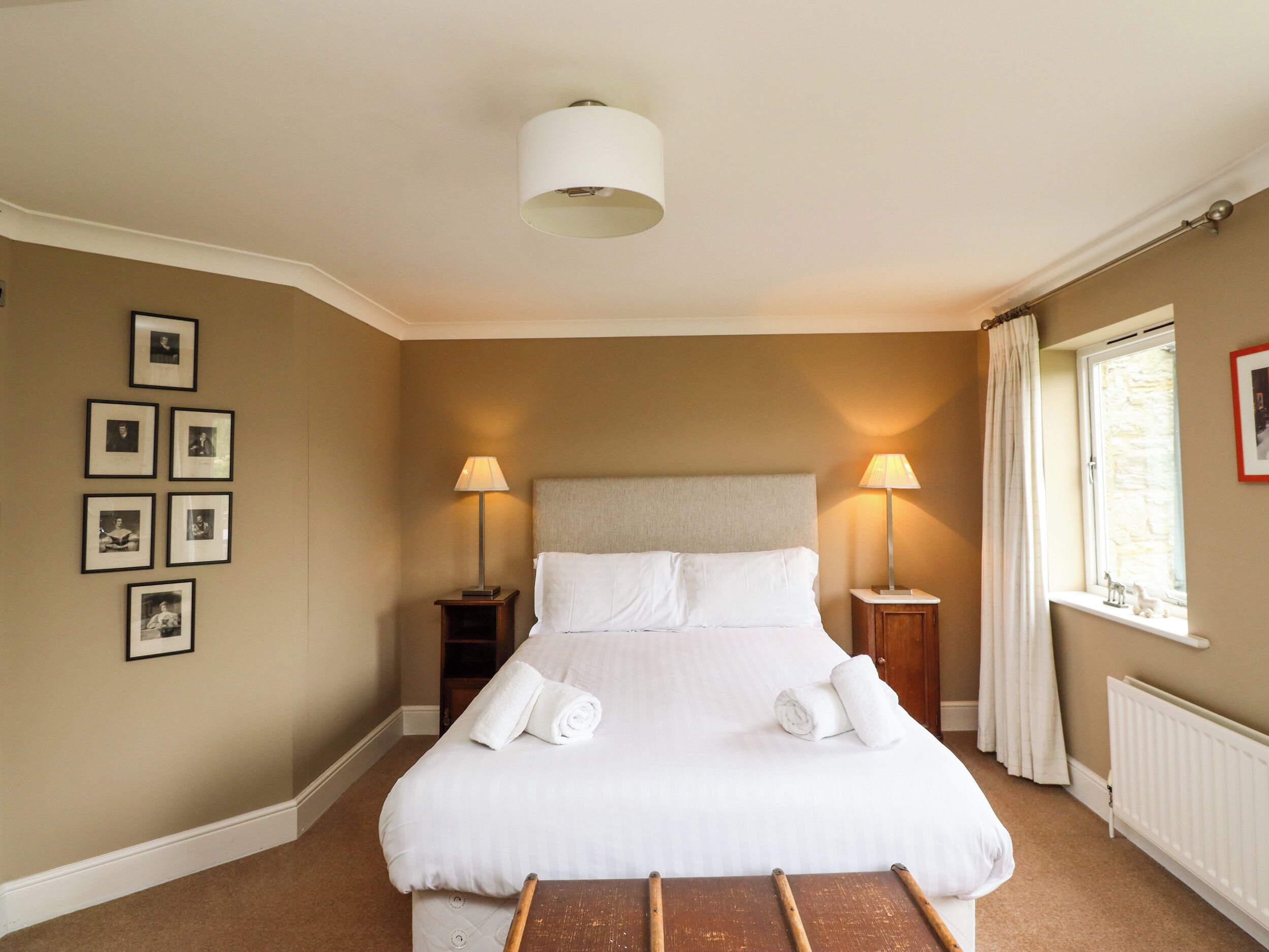 A neatly arranged bedroom with a large bed, two bedside tables, a ceiling light, and a window with curtains.