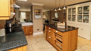 A kitchen with a central island, wooden cabinets, a black countertop, and hanging pendant lights. - The Book House (Morpeth)
