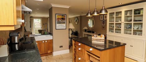 A kitchen with a central island, wooden cabinets, a black countertop, and hanging pendant lights.