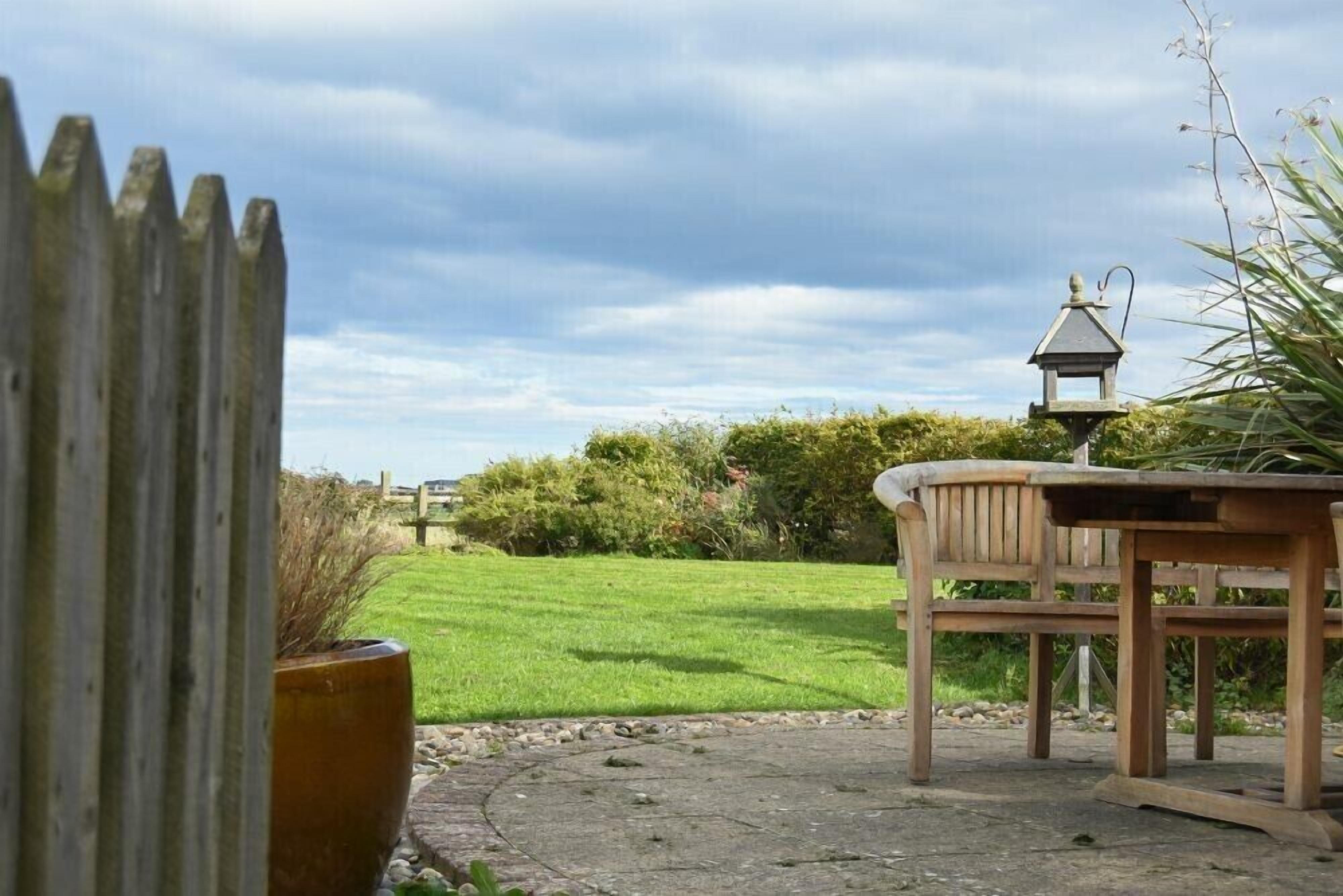 A wooden table and chair set on a concrete patio with a grassy lawn and a wooden fence in the background.