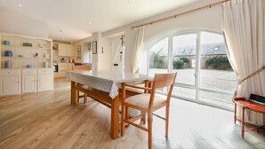 Eine geräumige Küche mit Holzboden, einem Esstisch mit Stühlen und einem großen Fenster mit Vorhängen.