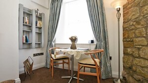 Ein gemütliches Zimmer mit einem runden Tisch, zwei Stühlen, einem Bücherregal, einer Vase und einer Stehlampe.