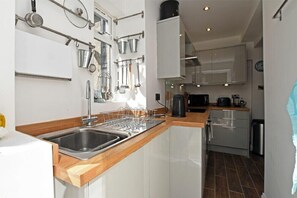 A modern kitchen with stainless steel appliances, wooden countertops, and a variety of cookware hanging on the wall. - Sea Air (Morpeth)