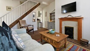 Ein Wohnzimmer mit Couch, Kamin, Fernseher und einer Holz-Kaffeetisch sowie einer Treppe.