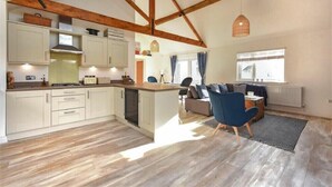 Une cuisine spacieuse avec des poutres en bois, un coin repas avec une chaise bleue et un salon avec un canapé.