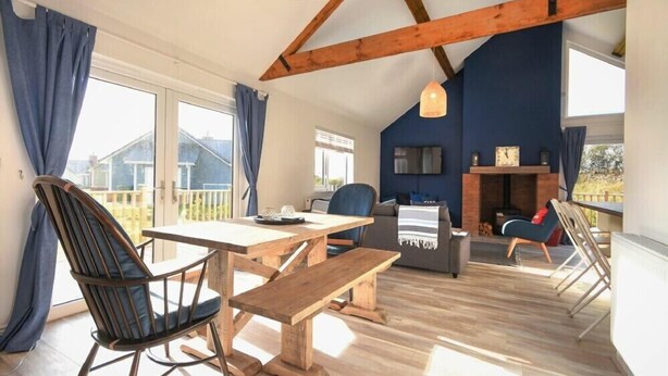 Une pièce spacieuse avec une table en bois, des bancs et un canapé. On y trouve une cheminée et un téléviseur fixé au mur.