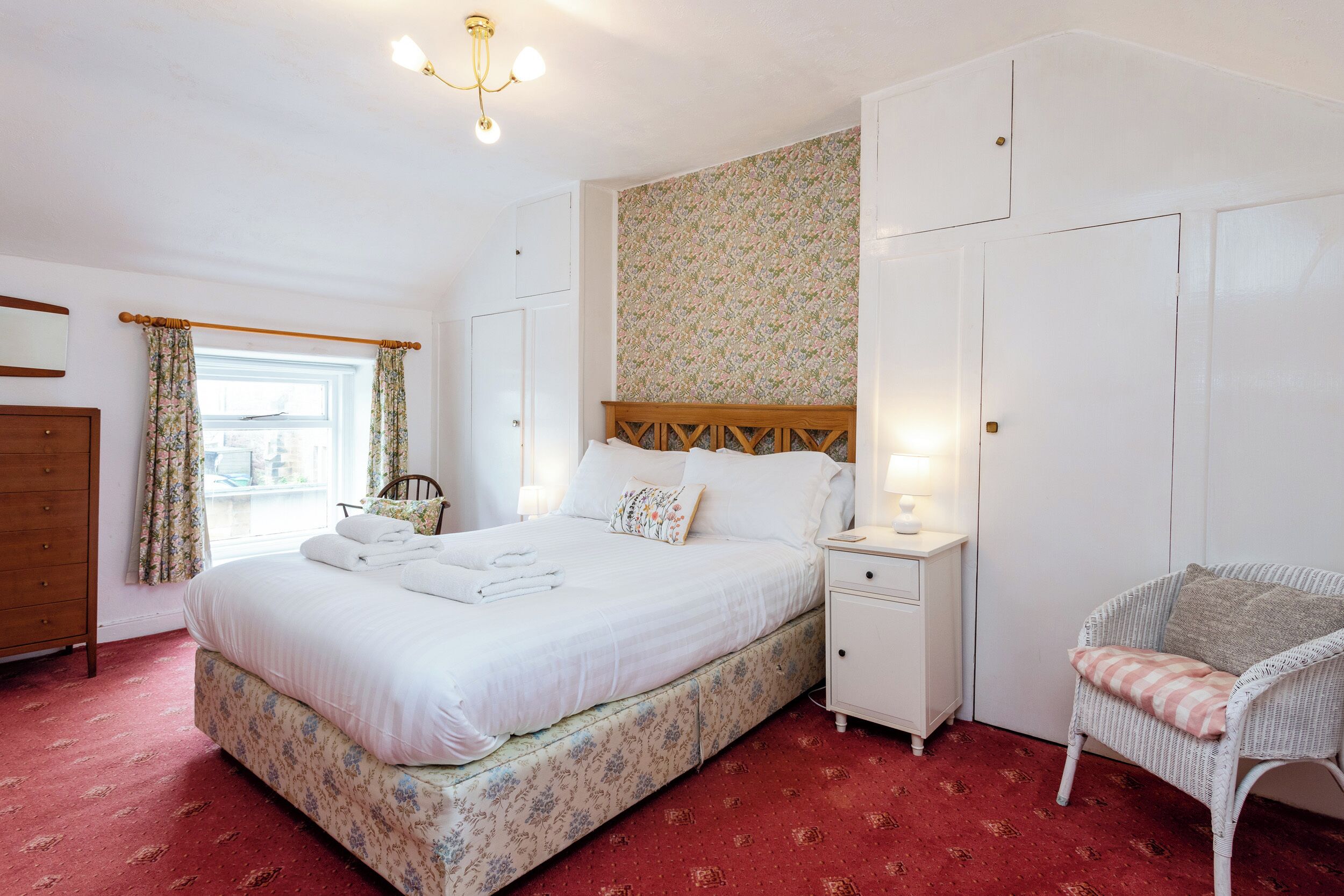 A bedroom with a large bed, a nightstand, a chair, and a wardrobe.