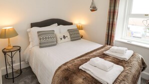 Un lit bien fait, avec des draps blancs et des coussins à motifs, une couverture marron moelleuse et des serviettes pliées au pied du lit.