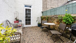 Une terrasse avec une porte blanche, une petite table et deux chaises en osier.