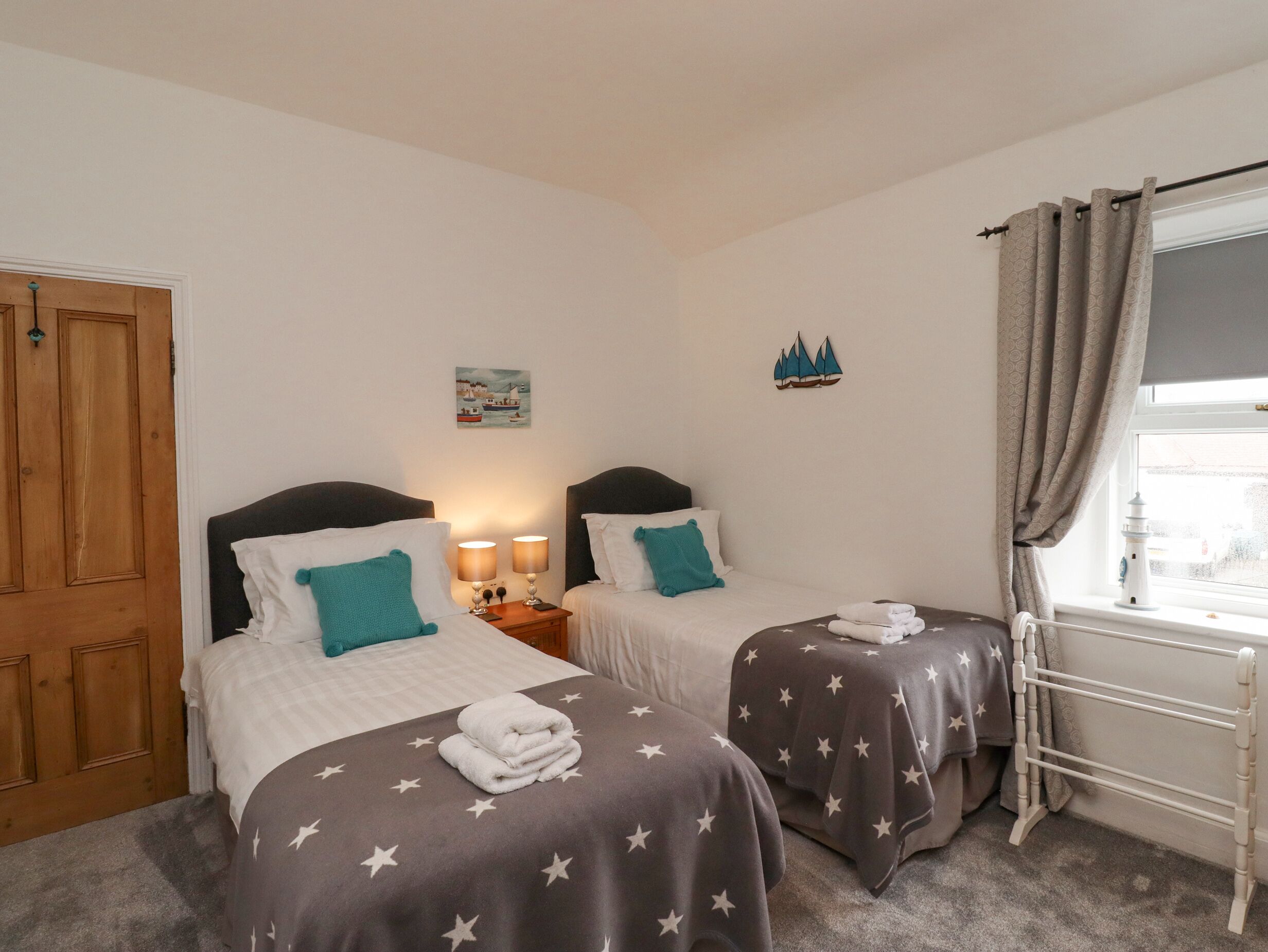 Een slaapkamer met twee eenpersoonsbedden, een houten garderobe, een nachtkastje met lampen, een schilderij en een raam met gordijnen.