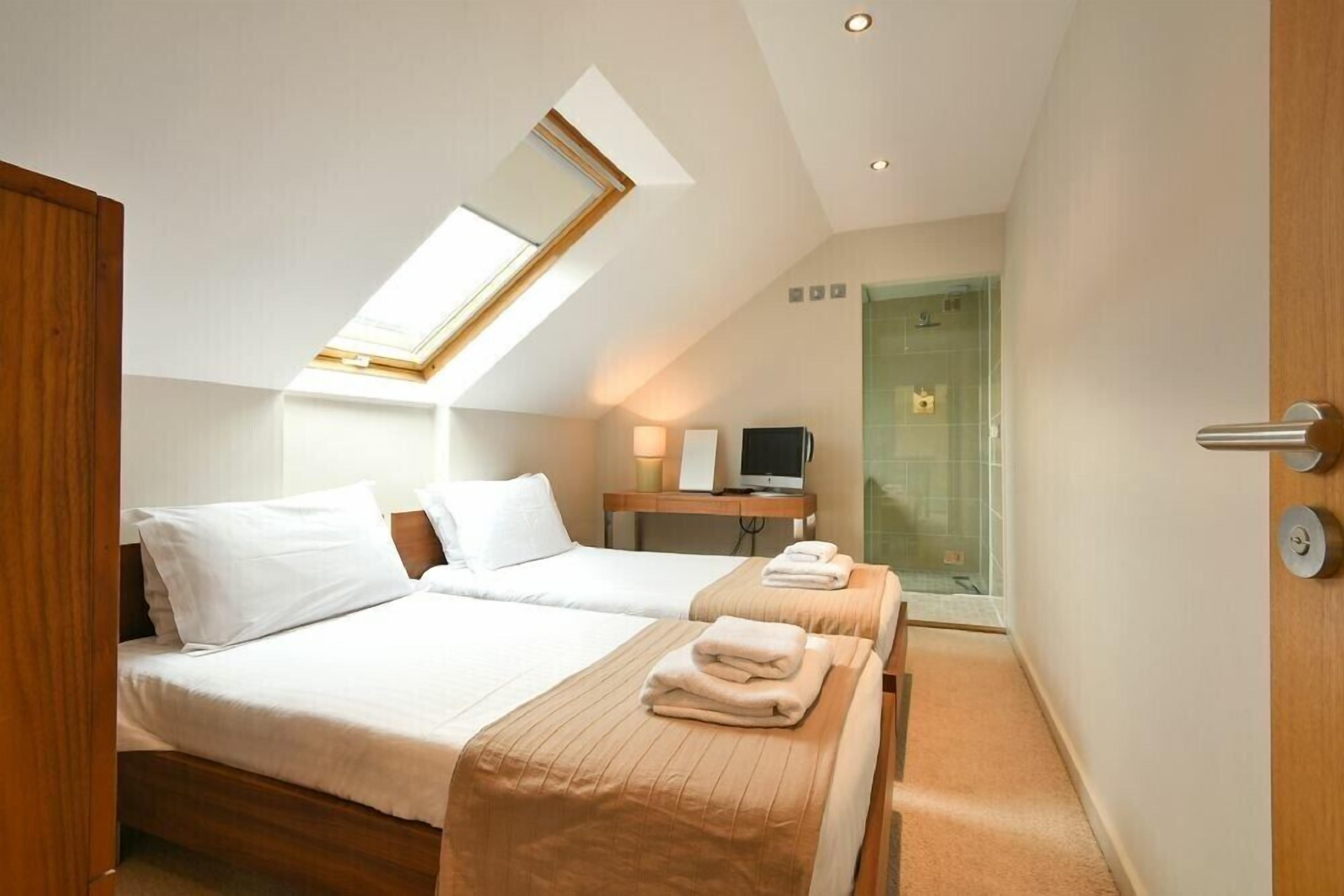 A bedroom with two beds, a skylight, a TV, and a glass shower area.
