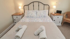 Un lit bien fait, avec une literie à motifs floraux, deux lampes de chevet, un ordinateur portable posé sur une table de chevet et une chaise en osier.