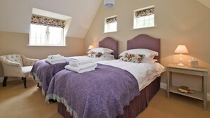 A bedroom with two beds, a chair, a nightstand, and a window with a curtain. - Sandpiper (Bamburgh)
