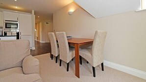 A dining area with a wooden table and four chairs, a sofa, and a kitchen in the background. - Sandpiper (Bamburgh)
