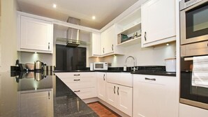 A modern kitchen with white cabinets, a black countertop, stainless steel appliances, and a built-in oven. - Sandpiper (Bamburgh)