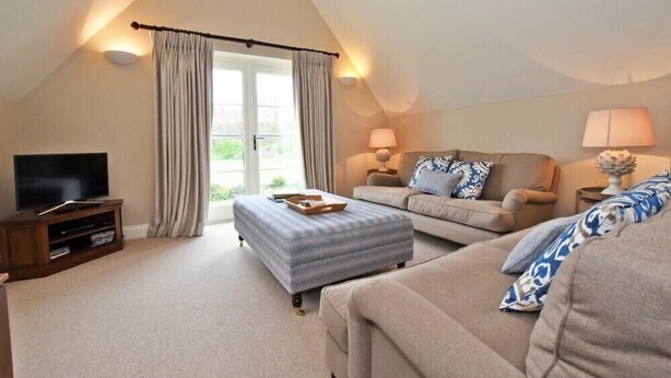 A cozy living room with a television, two sofas, a coffee table, and a window with curtains. - Sandpiper (Bamburgh)
