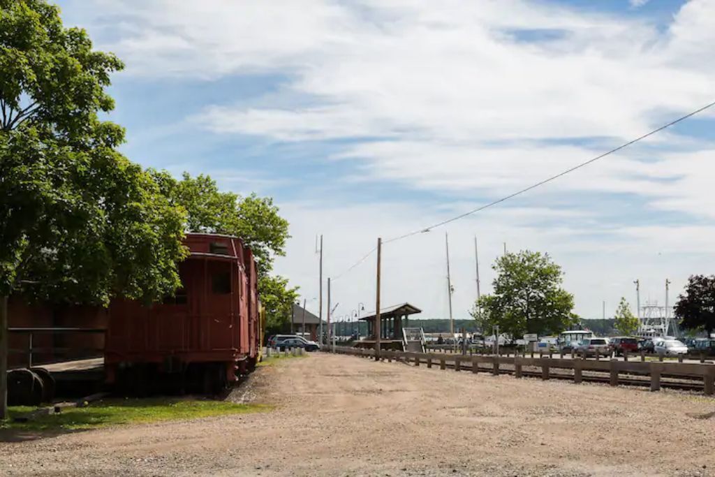 A gravel road leading to a red train car, with a wooden fence and trees on the left.