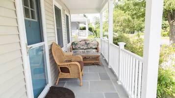 A covered porch with wicker furniture and a small table, a white railing, and a door with a number.