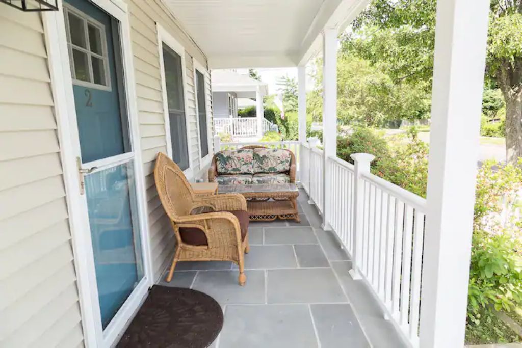 A covered porch with wicker furniture and a view of a green landscape.