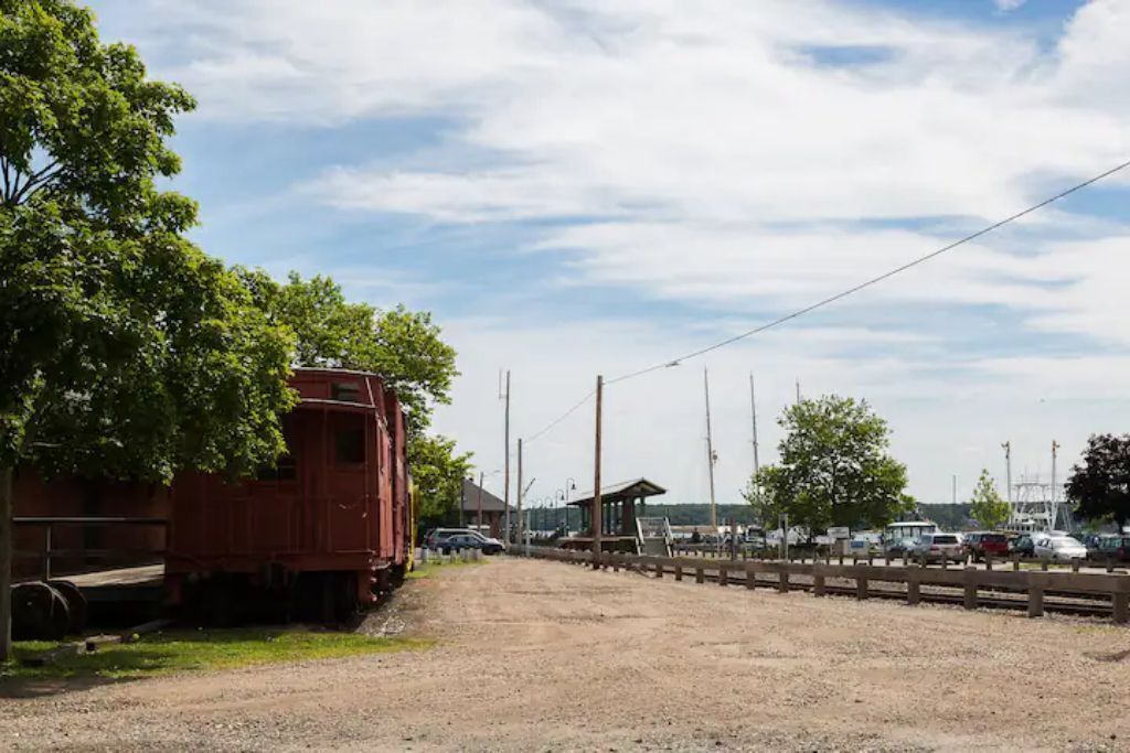 A gravel path leading to a red train car and a wooden fence.