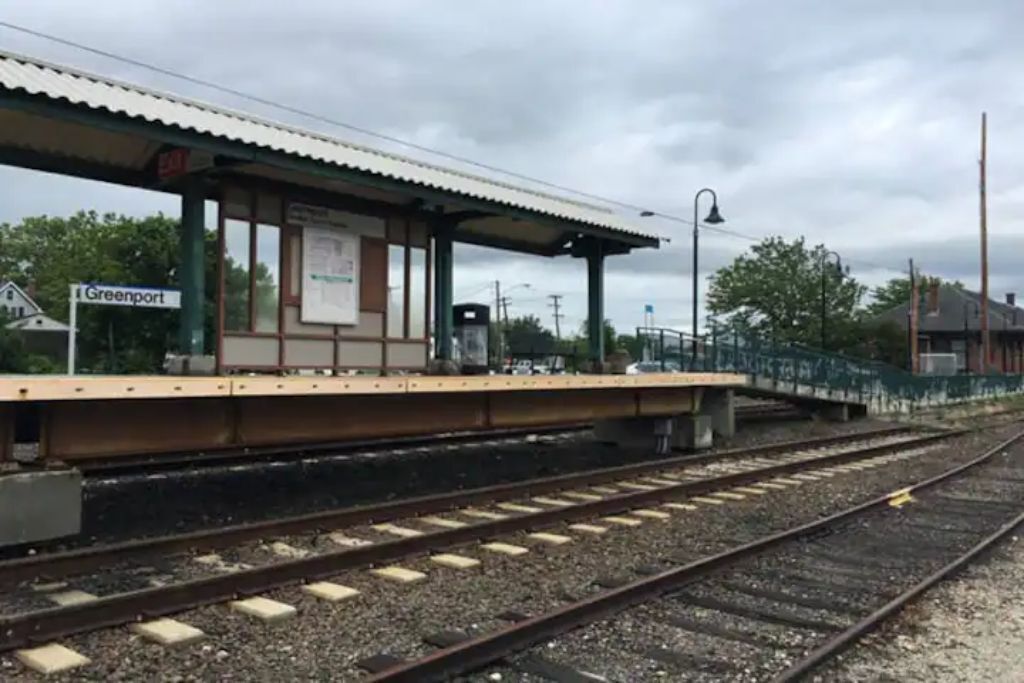 A train station platform with a shelter, a sign reading "Greenport," and multiple railway tracks.