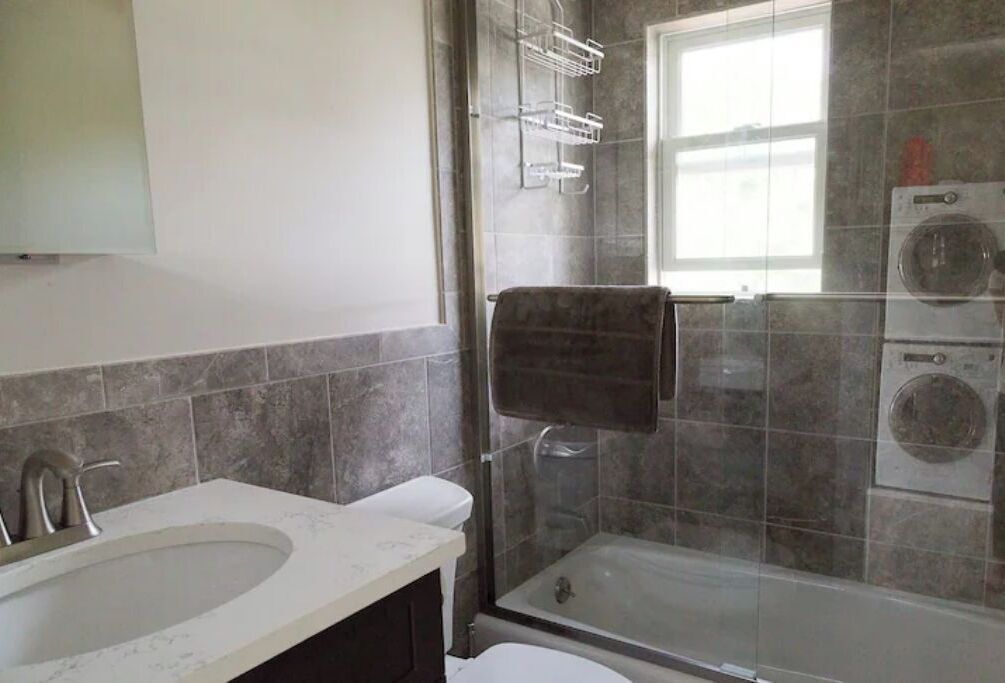 A bathroom with a sink, toilet, shower, and a washing machine.