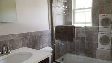 A bathroom with a sink, toilet, shower, and a washing machine.