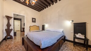 Una camera da letto con un letto in legno, un comodino, una lampada a parete e una porta che dà su un'altra stanza.