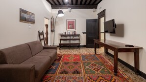 Un soggiorno con un divano marrone, un tavolino di legno, un tappeto decorato, una libreria e una TV montata a parete.