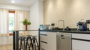 Une cuisine moderne équipée d’un lave-vaisselle, d’un grille-pain et d’une bouilloire sur le plan de travail. On y trouve également des tabourets de bar et une plante en pot sur le plan de travail.