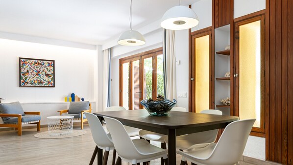 A modern dining area with a wooden table, white chairs, and pendant lights.