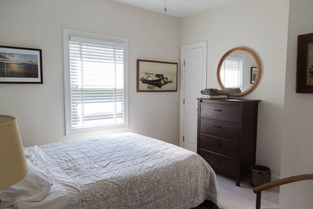 Un dormitorio con una cama, un aparador, un espejo y una ventana con persianas.