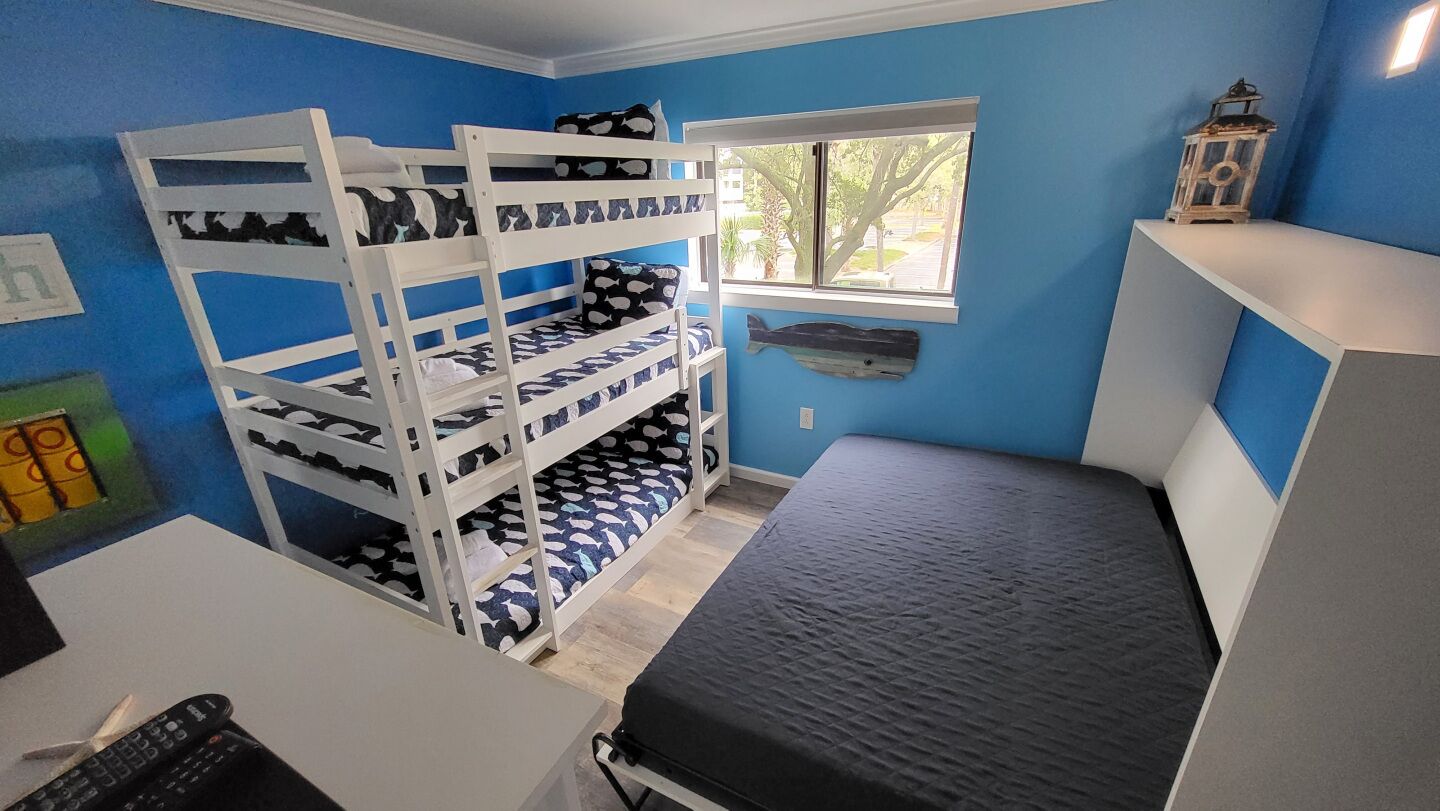 Une chambre avec des lits superposés, un bureau, une chaise, une fenêtre et une petite étagère sur laquelle se trouve une lanterne.