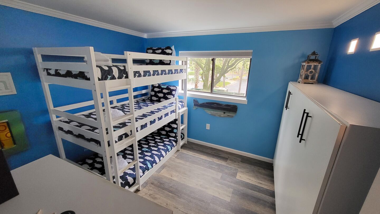 Een kamer met een stapelbed, een raam, een witte kast en een klein tafeltje.