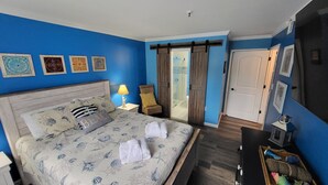 Una habitació d'hotel amb un llit, una tauleta de nit, una làmpada, una cadira i un escriptori amb una làmpada.