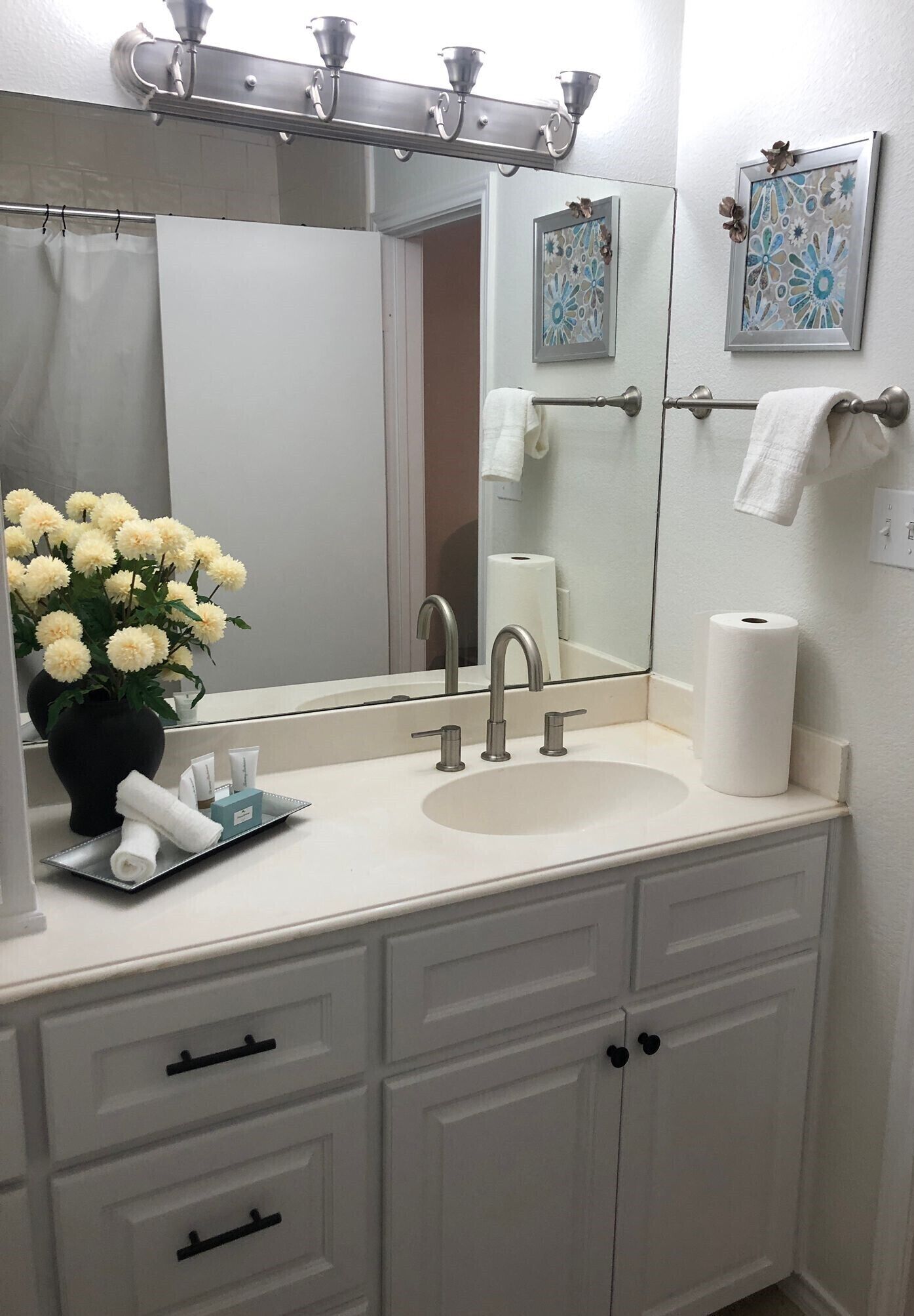 A bathroom with a white sink, a mirror, a towel rack, and a vase with flowers.