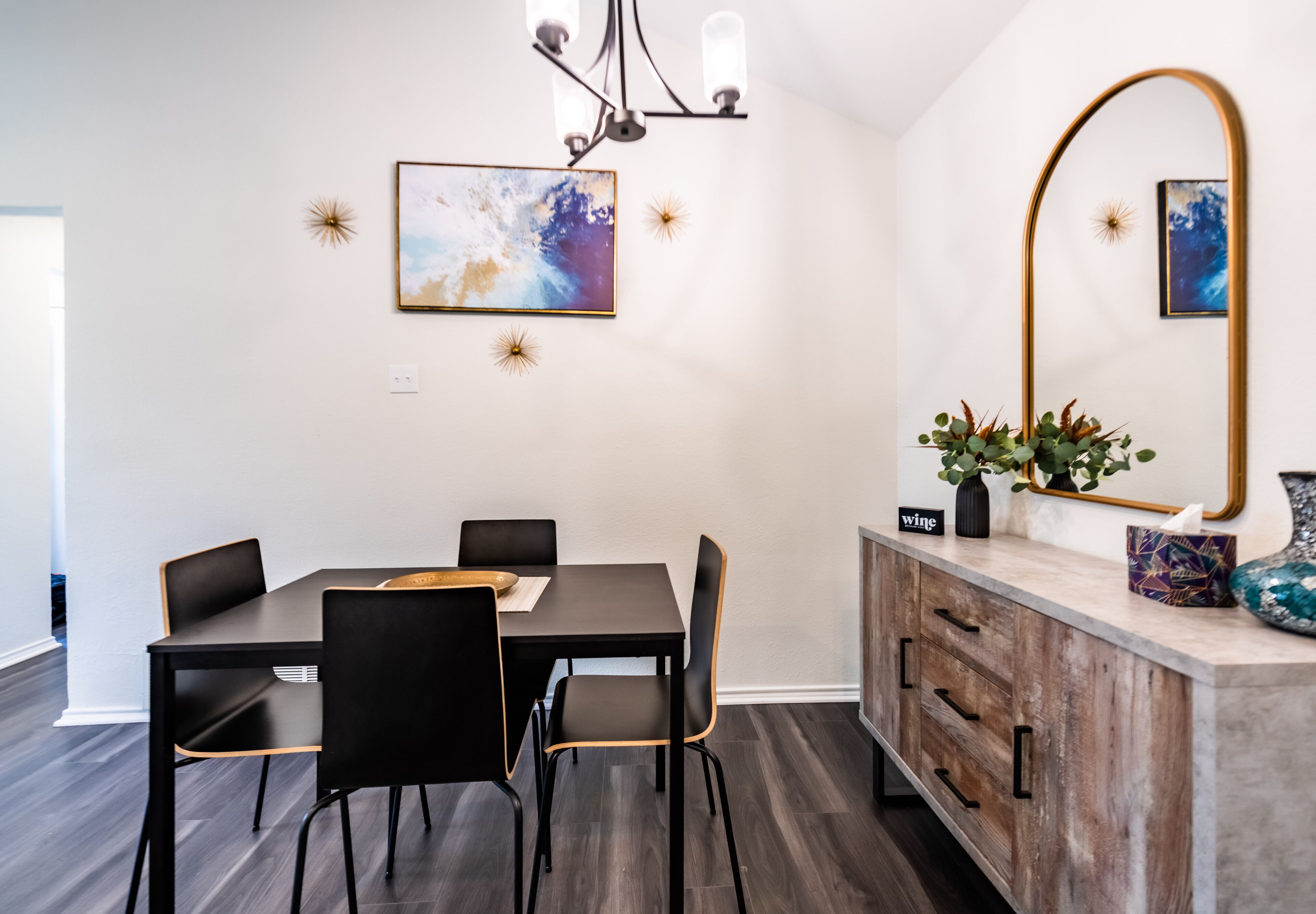Un coin repas avec une table et des chaises en bois foncé, un lustre moderne et des œuvres d’art accrochées au mur.
