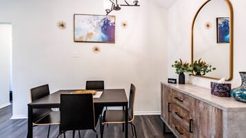 Un coin repas avec une table et des chaises en bois foncé, un lustre moderne et des œuvres d’art accrochées au mur.