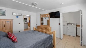 A bedroom with a bed, a dresser, a television, and a laundry area.