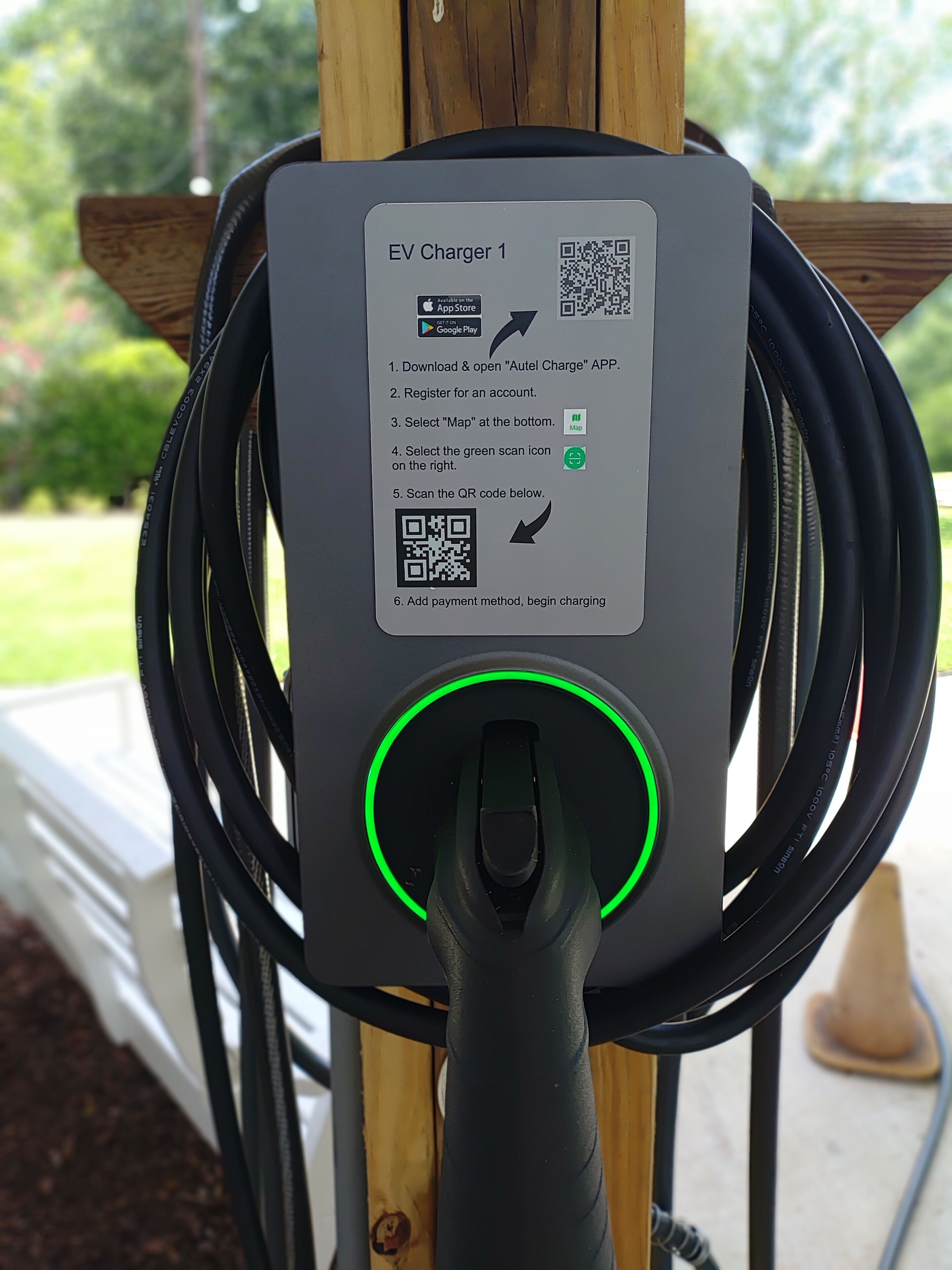 Eine EV-Ladestation mit Gebrauchsanweisung, einem QR-Code und einem grün beleuchteten Stecker.