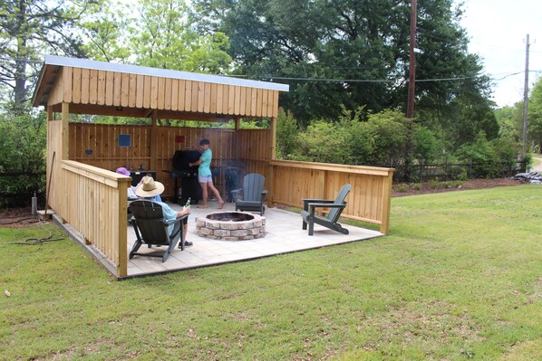 A wooden outdoor structure with a covered patio area, a fire pit, and seating.